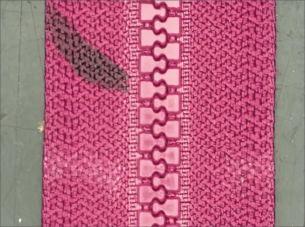 Source white-ring capture: interlocking zipper teeth and the adjacent pink fabric texture are visible. No slider or pull is demonstrated.